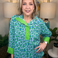 Woman wearing a green and blue patterned shirt in a home setting with lamps and artwork.