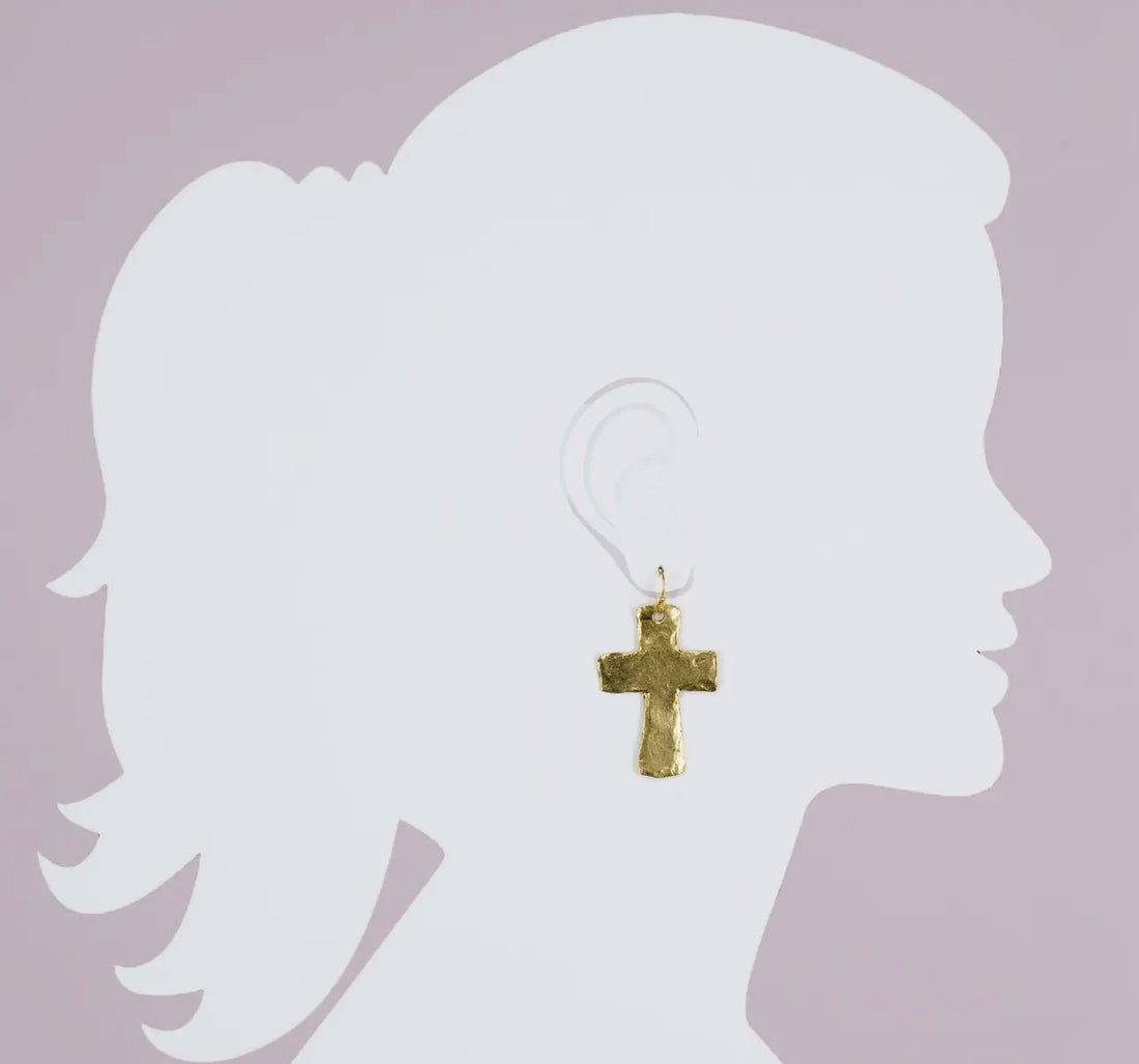 Gold cross earring on a silhouette of a person against a light purple background