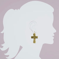 Gold cross earring on a silhouette of a person against a light purple background