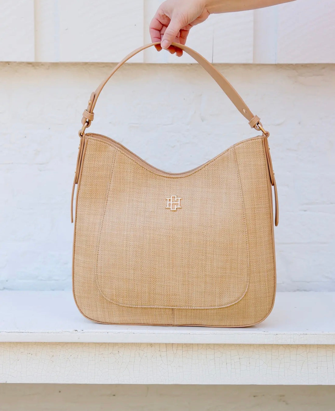 Beige handbag with a brand logo held by a hand against a light background