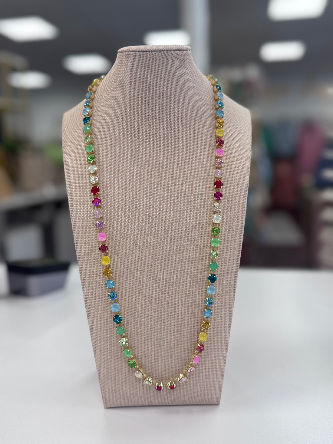 Multicolored gemstone necklace on a mannequin bust with a blurred indoor background