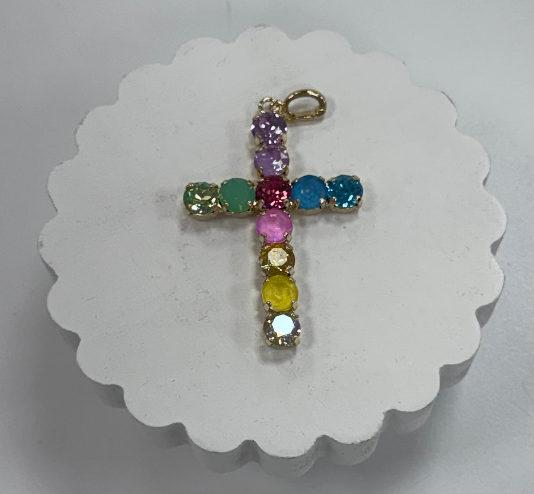 Cross-shaped pendant with colorful gemstones on a white scalloped card