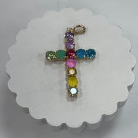 Cross-shaped pendant with colorful gemstones on a white scalloped card