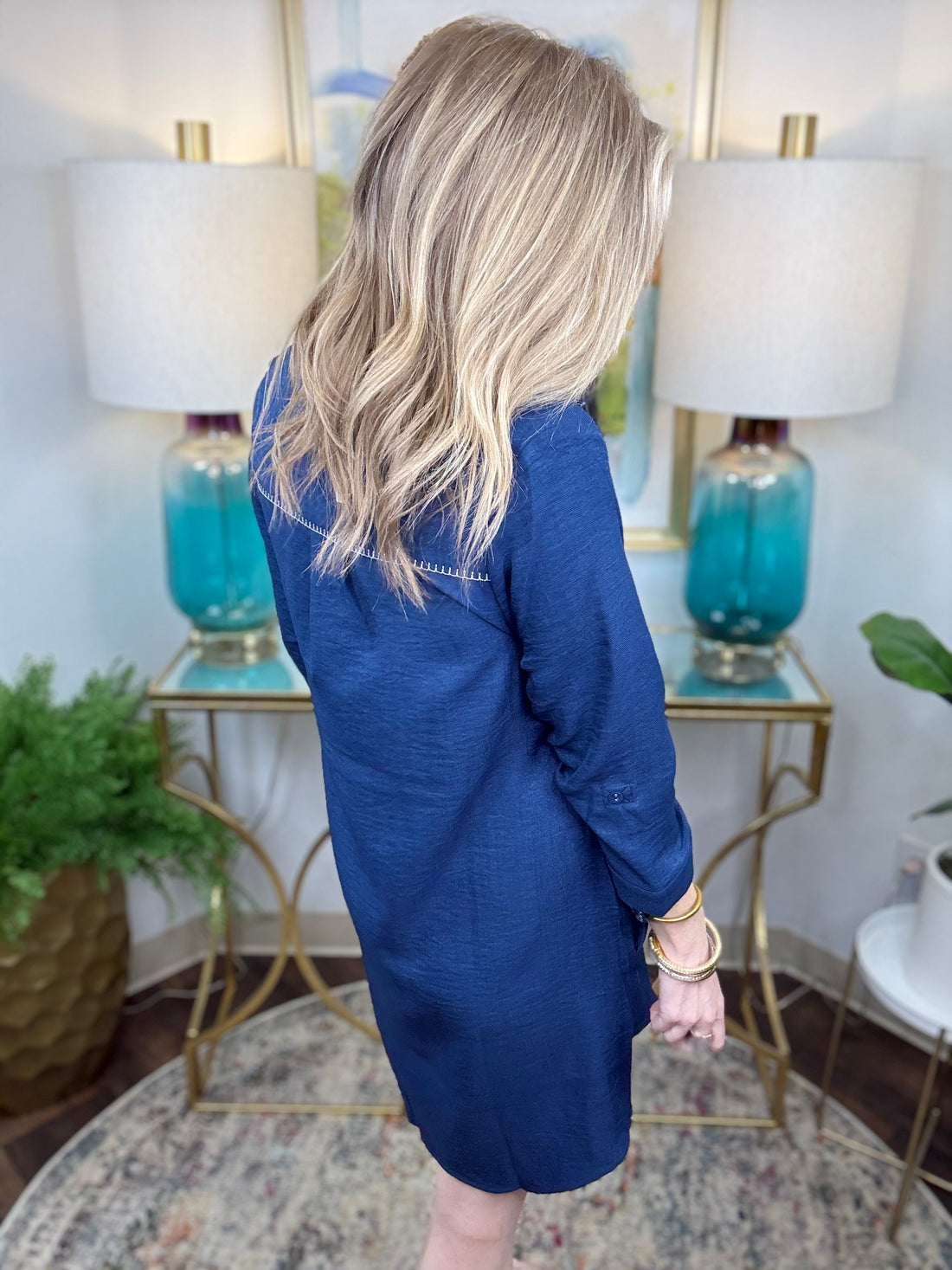 Woman wearing a navy shirt dress in a home setting with lamps and decor.