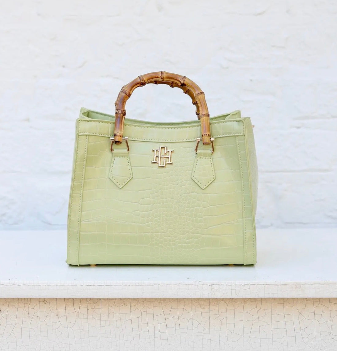 Light green handbag with wooden handle on a textured white surface