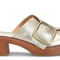 A single women's clog sandal with a metallic silver strap, a large gold-tone buckle, and a brown wooden platform heel, shown from a side profile on a white background.