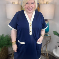 Woman wearing a navy nautical style blue dress with cream trim and gold buttons