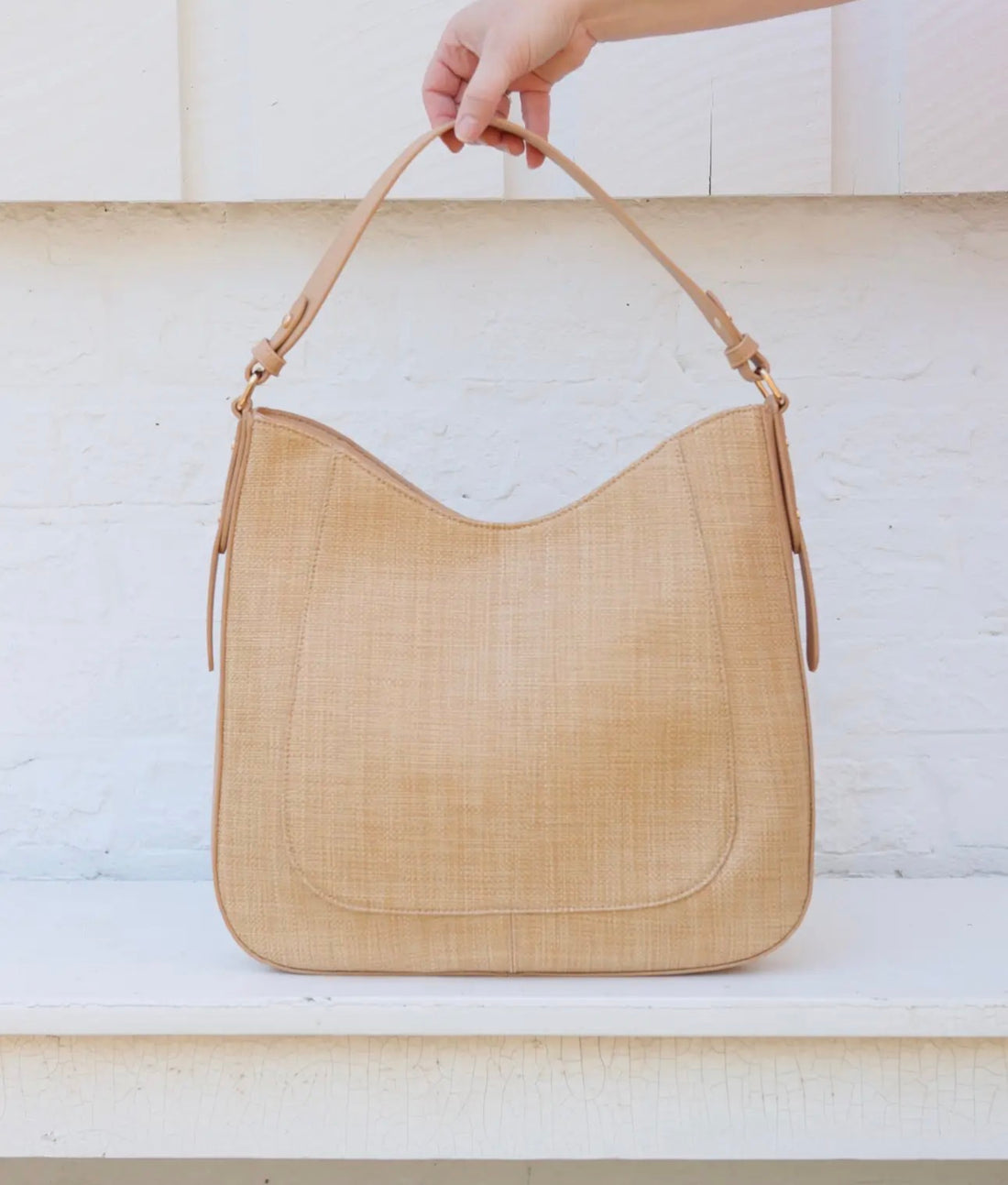 Beige handbag held by a hand against a light background