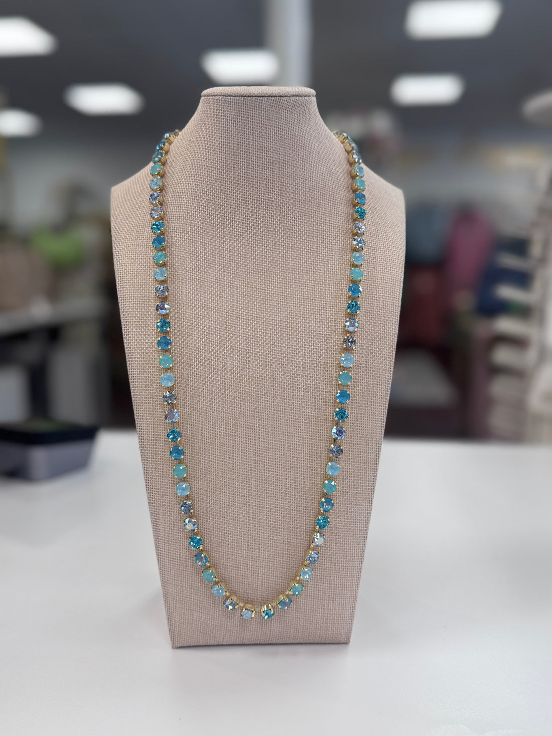 Blue gemstone Necklace on a mannequin bust with a blurred indoor background