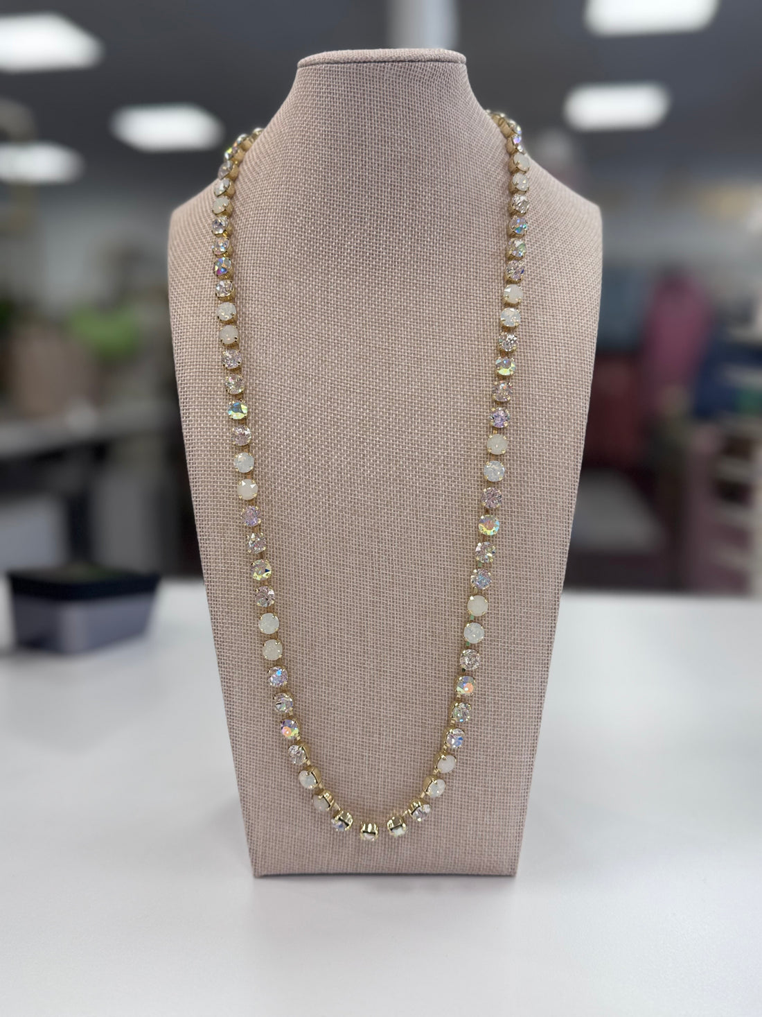 Opal-style white and clear stoned necklace on a mannequin bust with a blurred indoor background