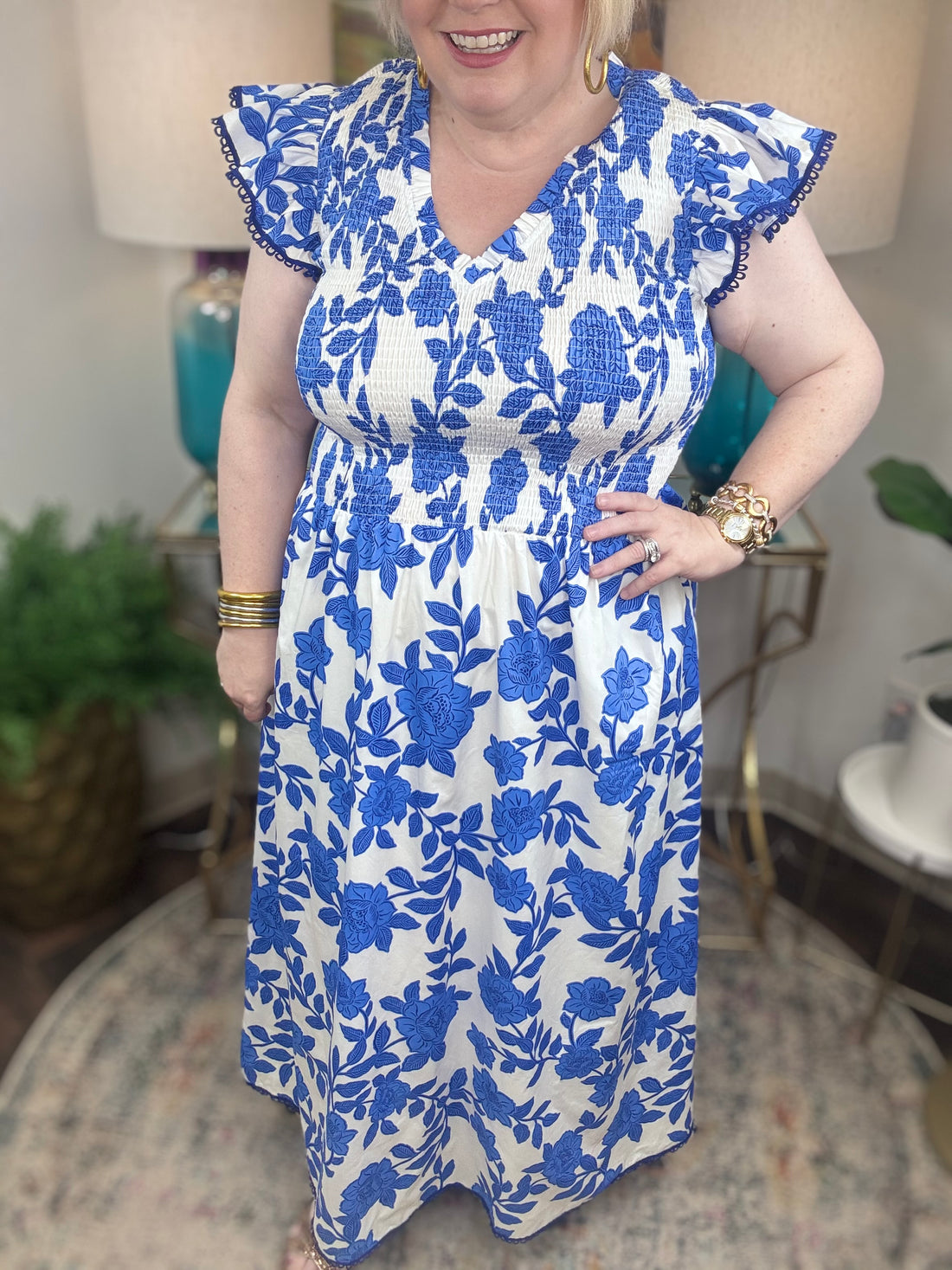 A woman with blonde hair wearing a white and blue floral print maxi dress with smocked bodice and ruffled cap sleeve