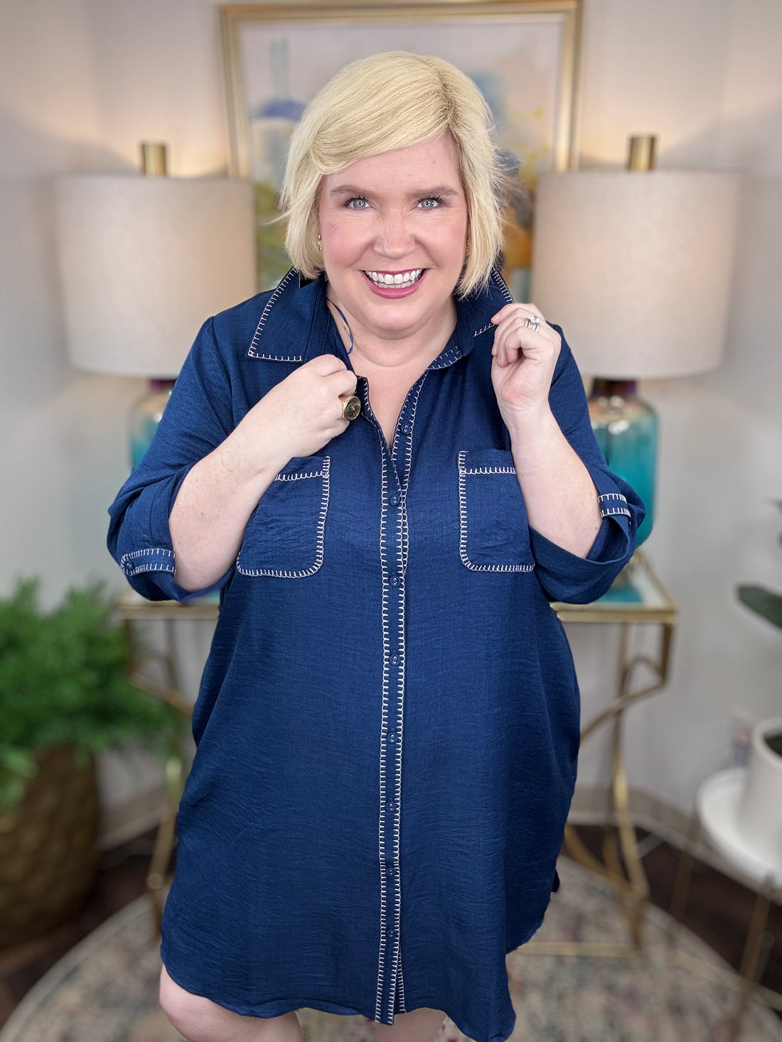 Woman wearing a navy shirt dress in a home setting with lamps and decor.