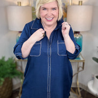 Woman wearing a navy shirt dress in a home setting with lamps and decor.
