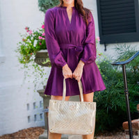 Woman in a purple dress holding a metallic champagne handbag outdoors.
