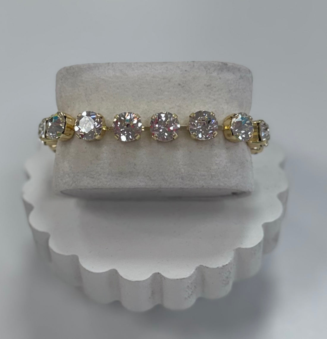 Gold and diamond bracelet on a white stand with a gray background