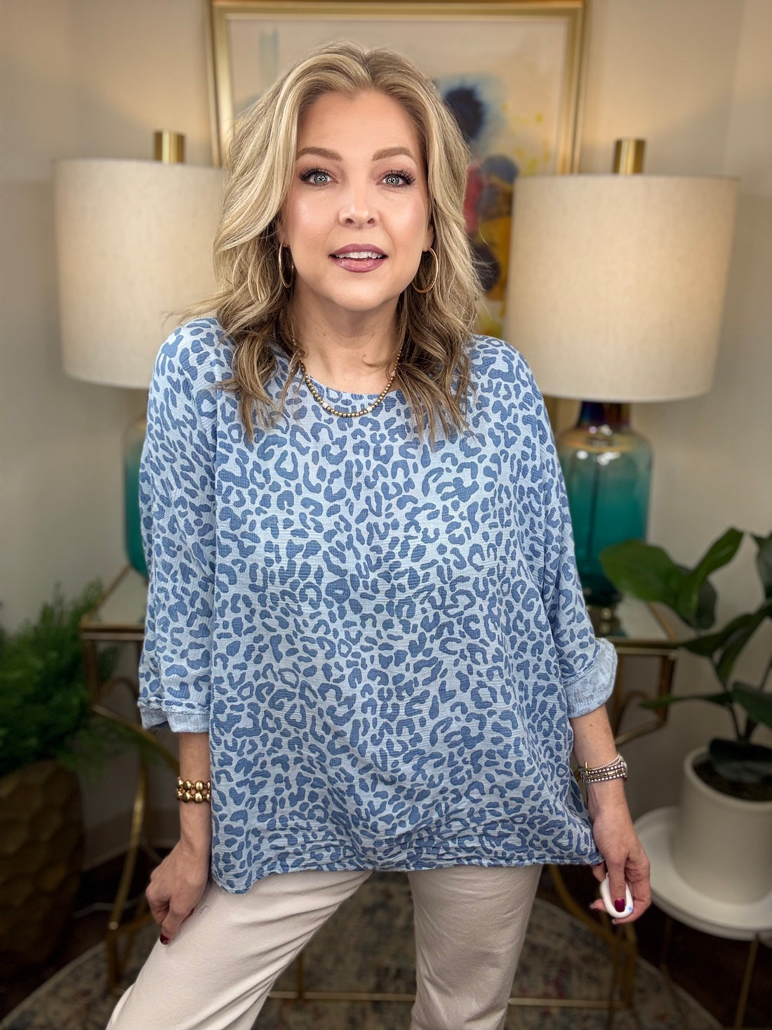Woman wearing a blue leopard print top in a home setting with lamps and plants.