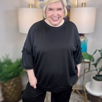Woman wearing a black matching set with bows tied on the sleeves.