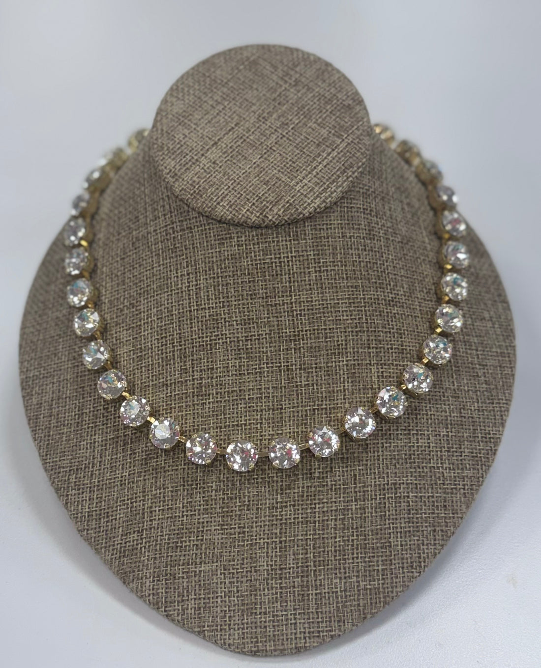 Necklace with clear stones on a brown textured stand against a white background