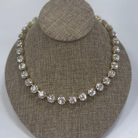Necklace with clear stones on a brown textured stand against a white background