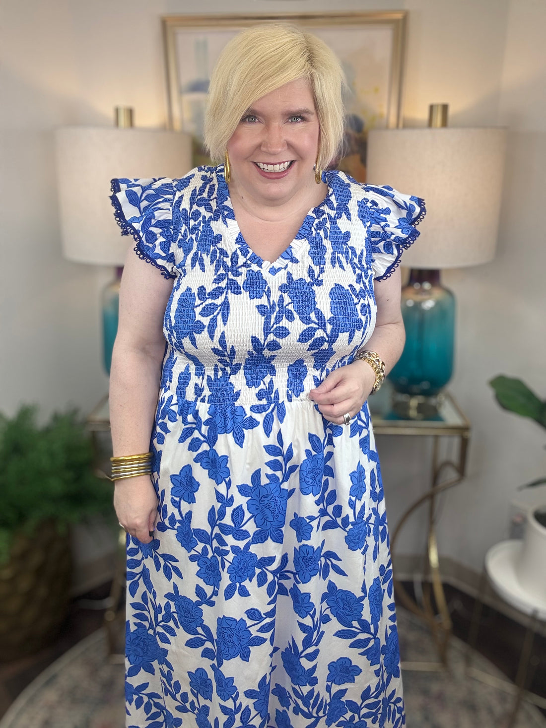 A woman with blonde hair wearing a white and blue floral print midi dress with smocked bodice and ruffled cap sleeve