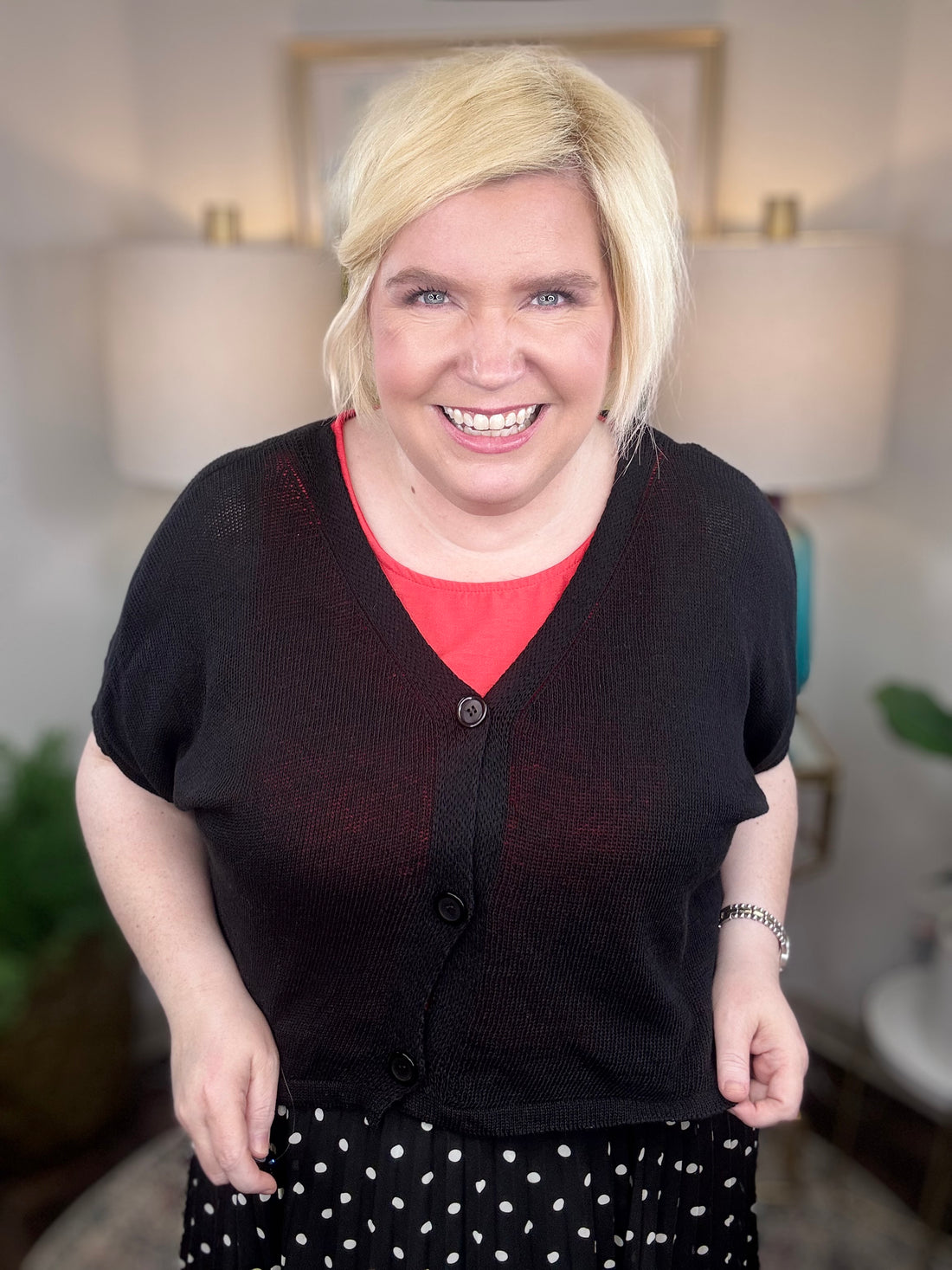 Woman wearing a black cardigan and polkadot print skirt indoors.