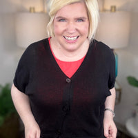 Woman wearing a black cardigan and polkadot print skirt indoors.