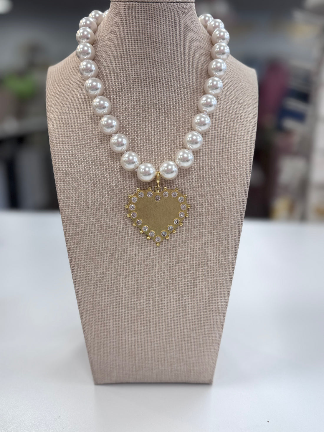 Pearl necklace with a heart-shaped pendant on a gray bust