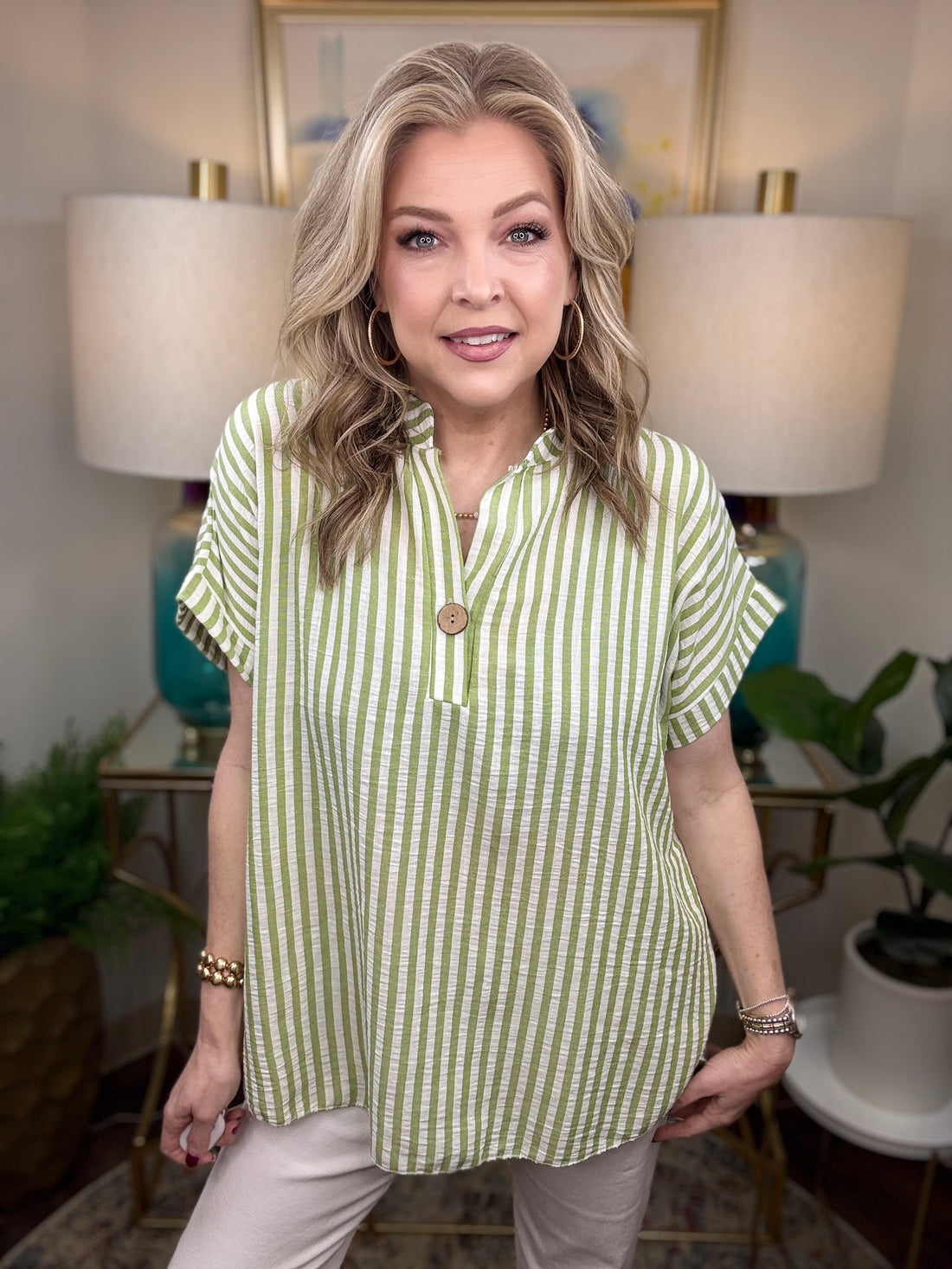 Woman wearing a green and white striped shirt in a home setting with lamps and plants.