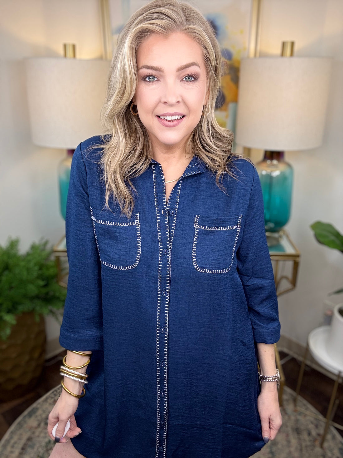 Woman wearing a navy shirt dress in a home setting with lamps and decor.