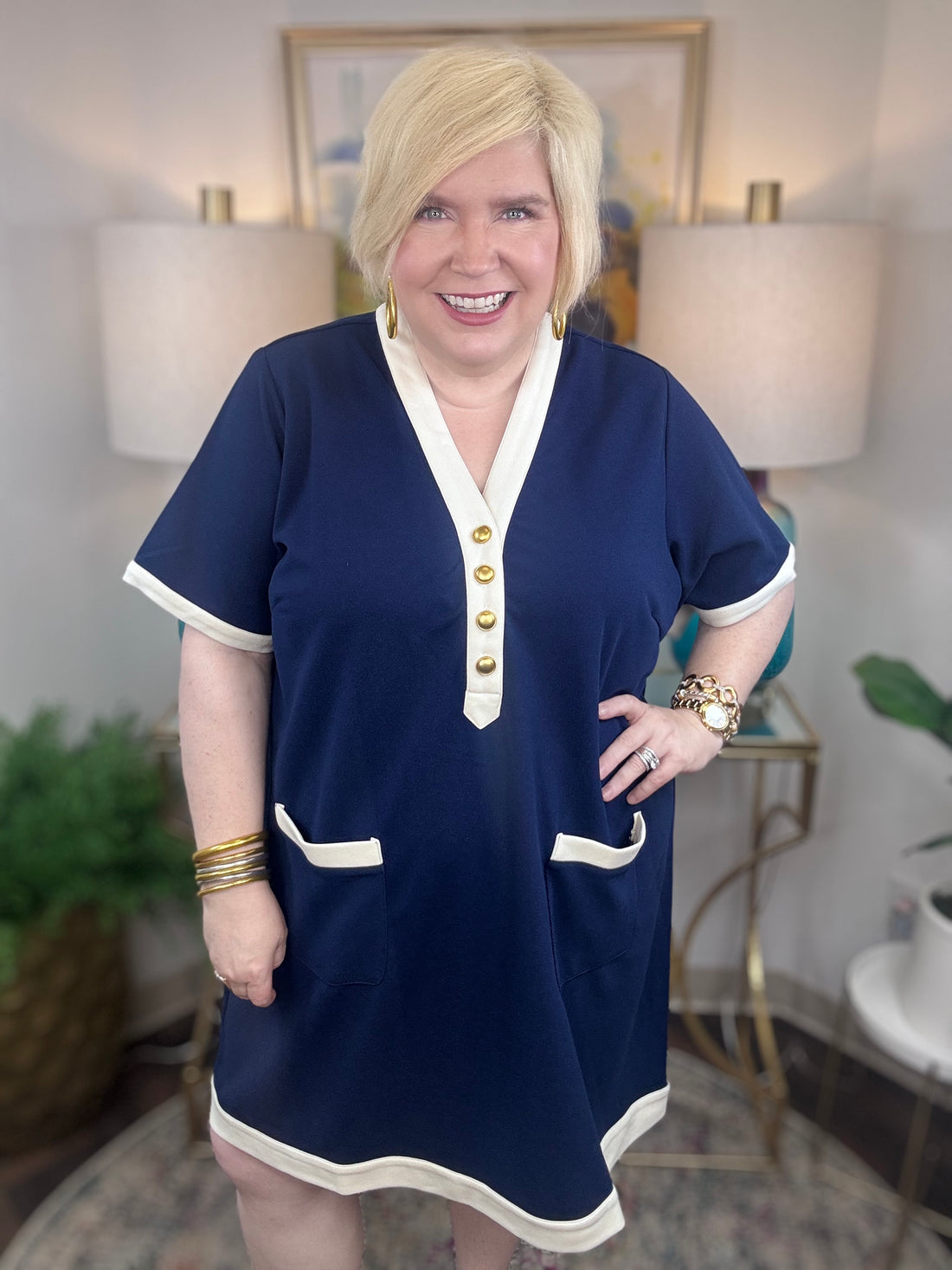 Woman wearing a navy nautical style blue dress with cream trim and gold buttons