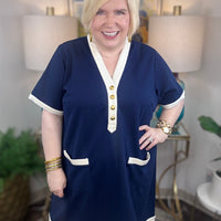 Woman wearing a navy nautical style blue dress with cream trim and gold buttons