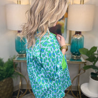 Woman wearing a green and blue patterned shirt in a home setting with lamps and artwork.