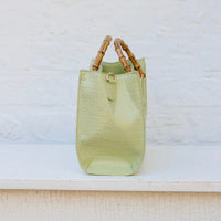 Light green handbag with bamboo handles on a textured surface