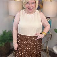 Woman wearing a beige top and brown polka dot skirt indoors.
