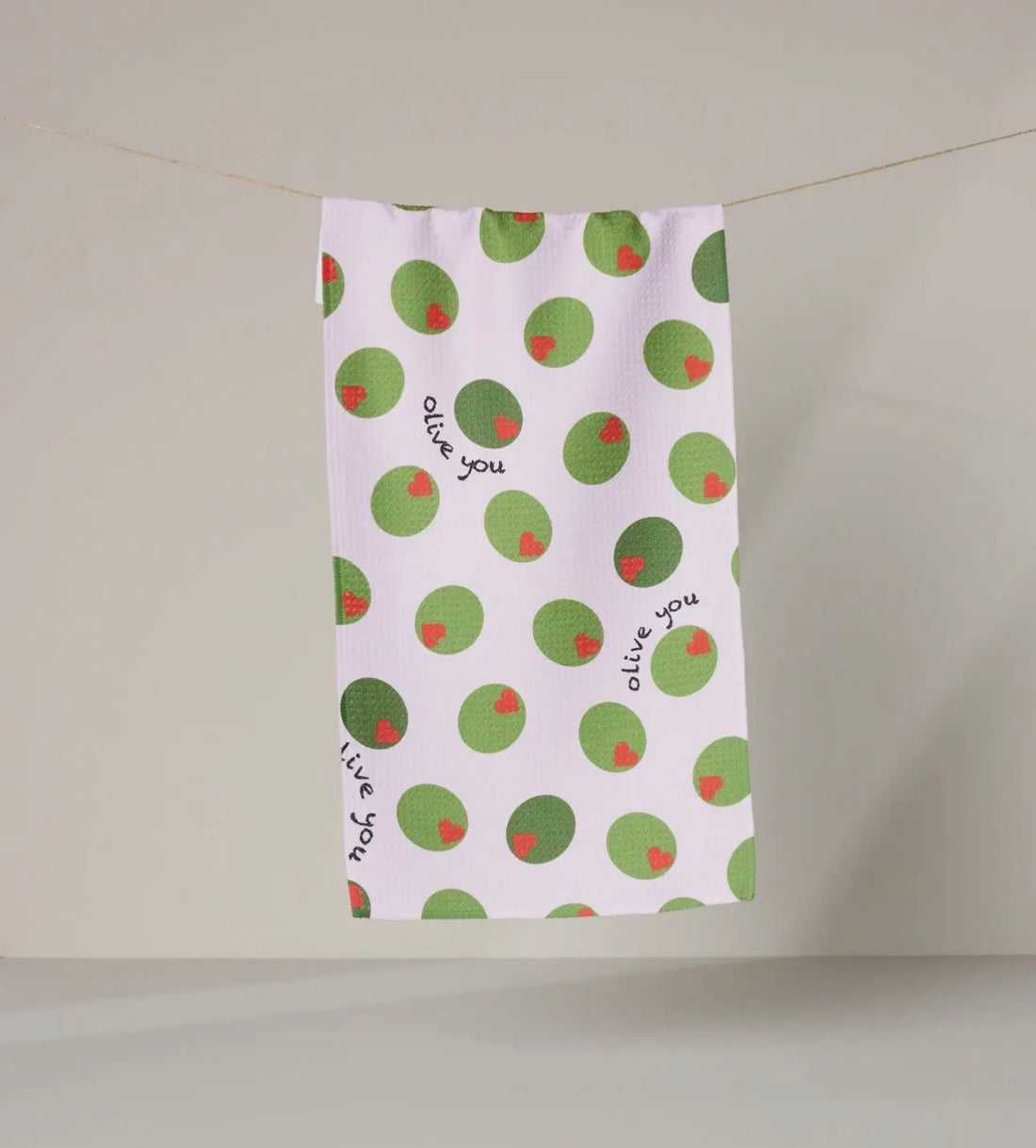 Tea towel with green olive pattern and text on a light pink towel