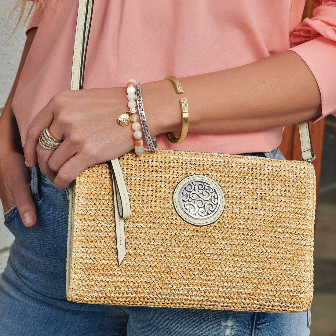 Person holding a yellow woven handbag with a decorative clasp, wearing a pink top and blue jeans.
