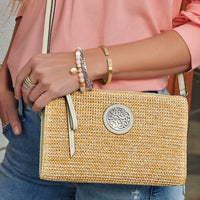 Person holding a yellow woven handbag with a decorative clasp, wearing a pink top and blue jeans.