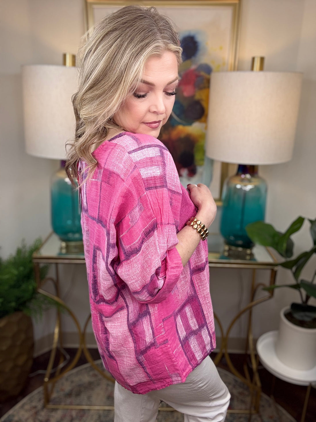 Woman wearing a pink patterned top in a room with lamps and a painting.