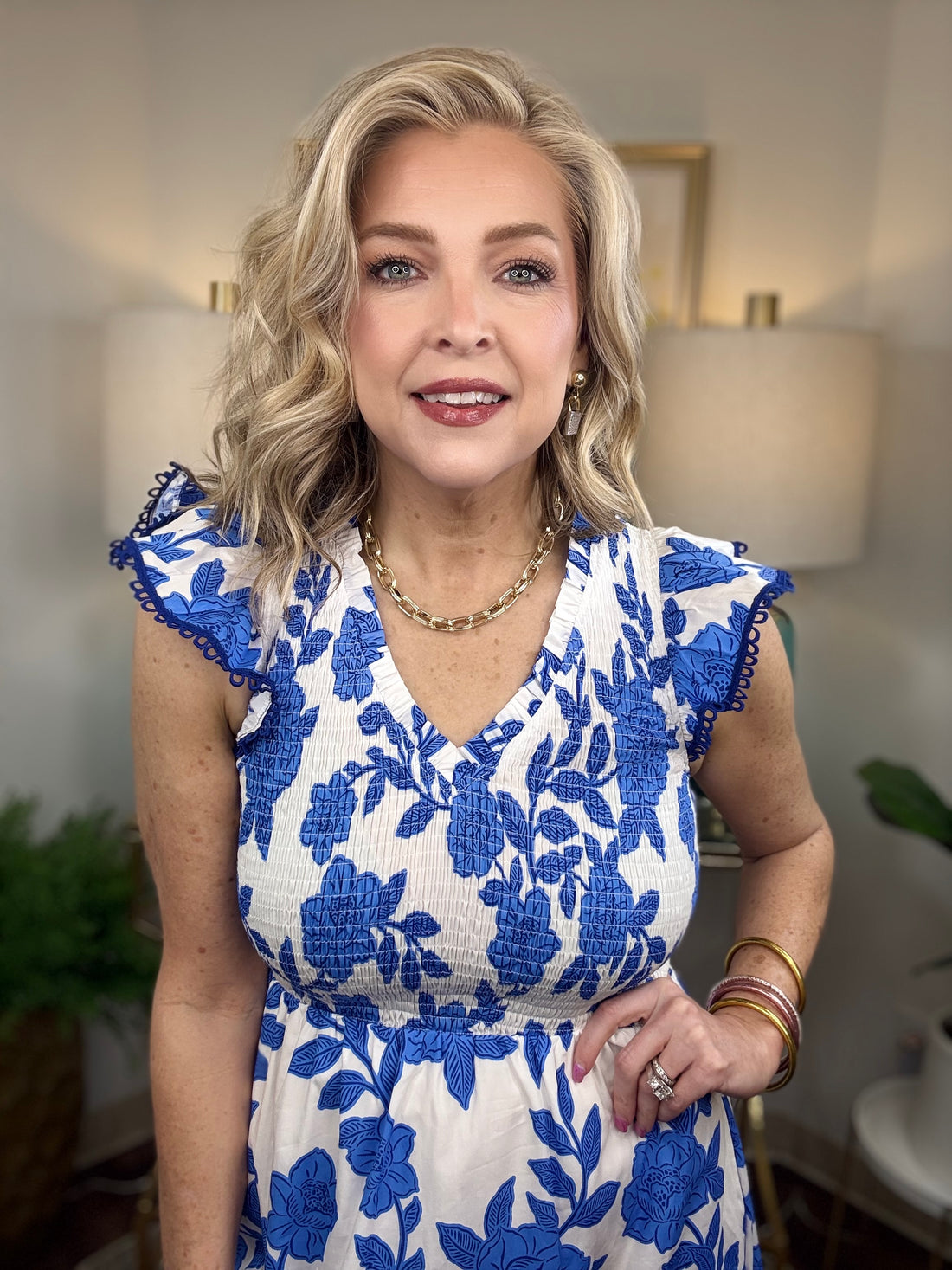 A woman with blonde hair wearing a white and blue floral print maxi dress with smocked bodice and ruffled cap sleeve