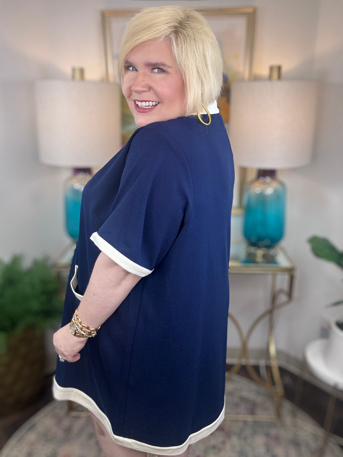 Woman wearing a navy nautical style blue dress with cream trim and gold buttons