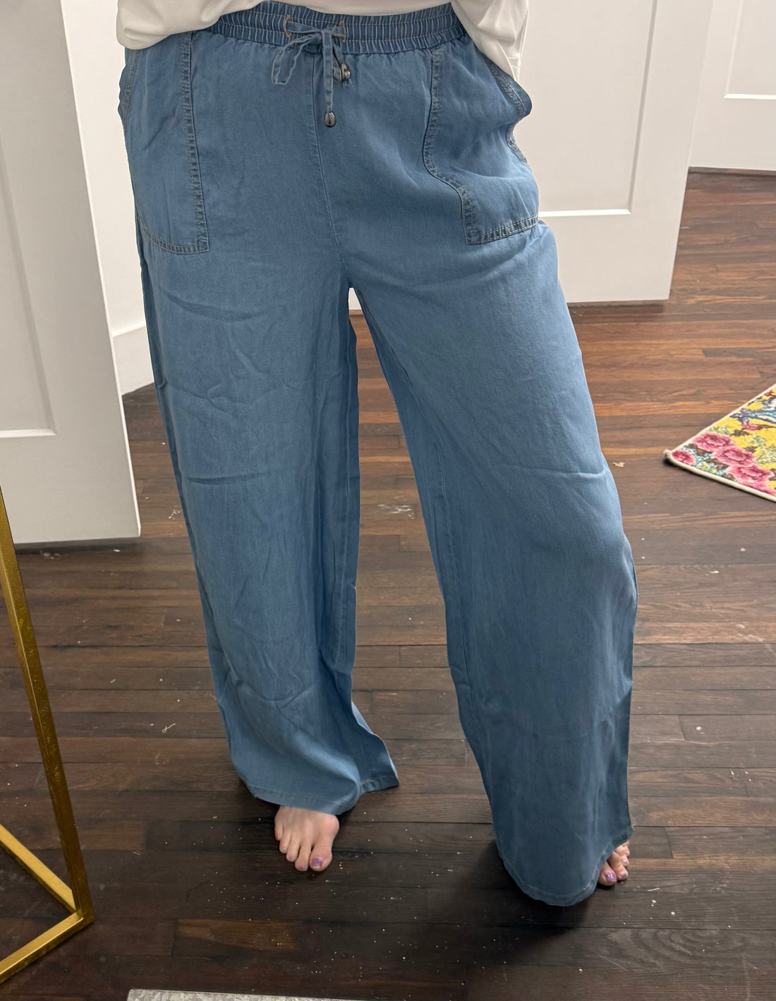 Person wearing blue wide-leg pants standing on a wooden floor.