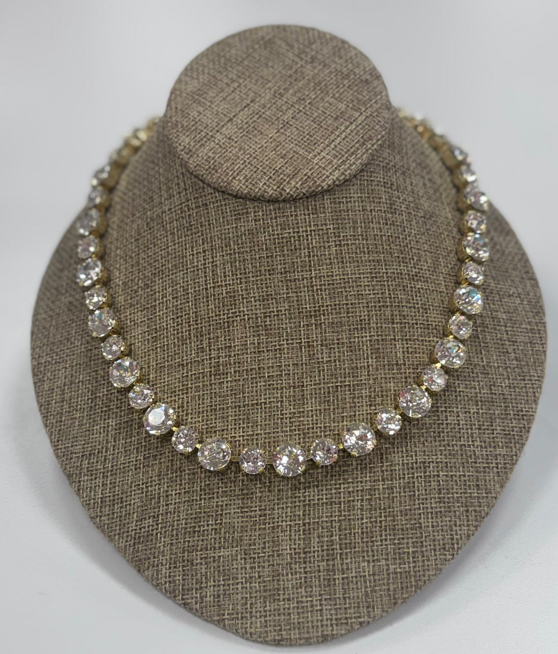 Necklace with clear stones on a brown textured stand against a white background