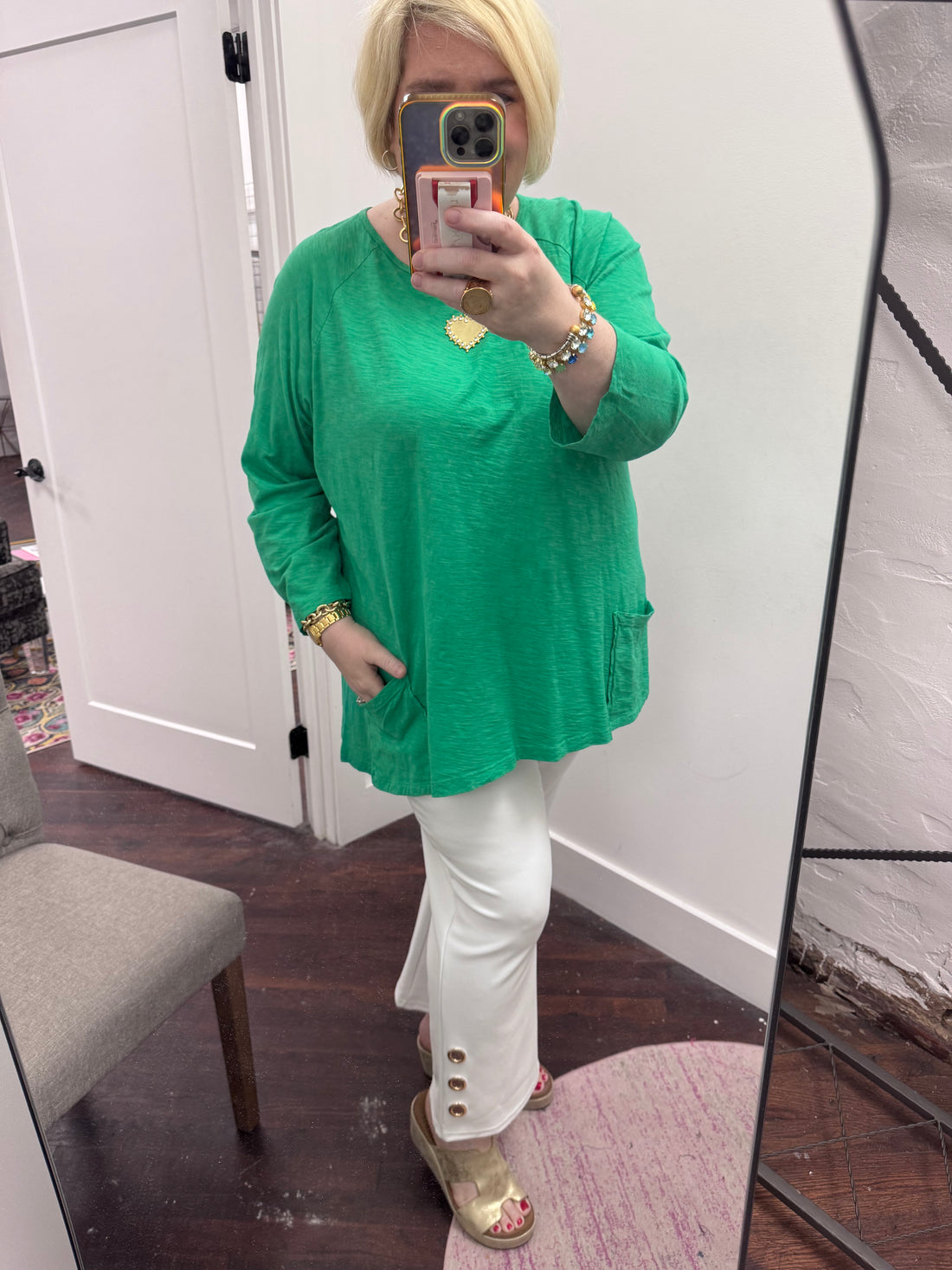 Person wearing a green top and white pants taking a mirror selfie.