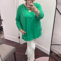Person wearing a green top and white pants taking a mirror selfie.