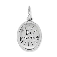 Silver pendant with 'Be present' engraving on a white background