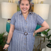 Woman wearing a blue dress with a belt, standing in a room with lamps and artwork.