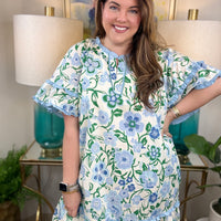 Woman wearing a blue and white ruffled dress with greenery accents.