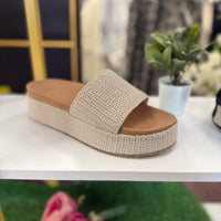Beige sandal with brown sole on a white surface, blurred background