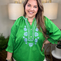 Woman wearing a green blouse with blue floral embroidery