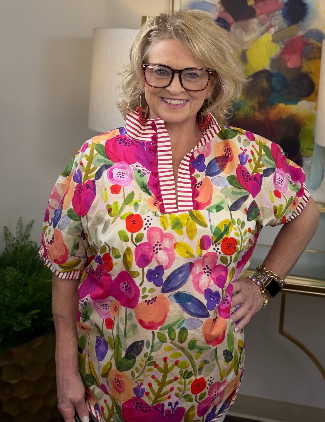 Woman wearing a colorful floral top with a striped collar in an indoor setting.